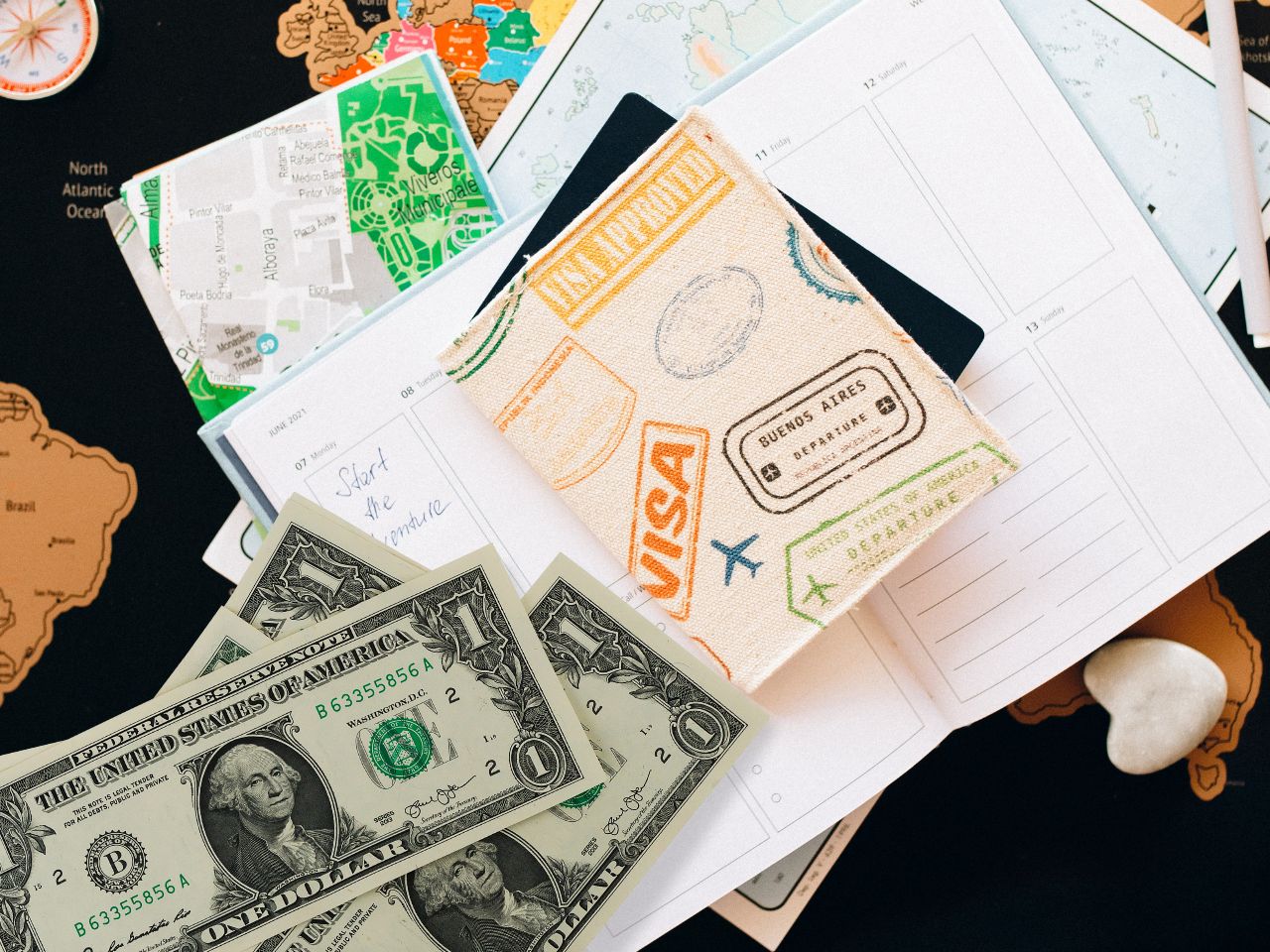 U.S. dollar bills, a travel planner, and a passport cover with visa and departure stamps, symbolizing travel and immigration-related expenses and planning—relevant to changes in the Diversity Visa Lottery program. Ask ChatGPT