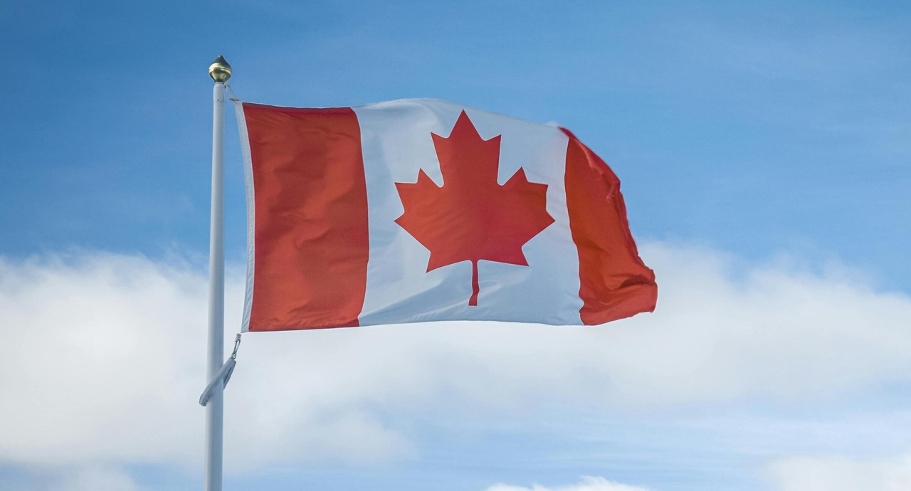 Canadian flag waving on a flagpole against a blue sky with light clouds.
