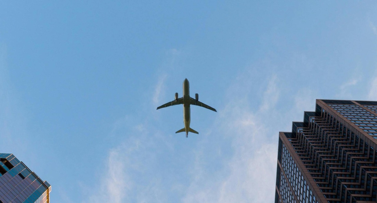 An airplane flying above tall buildings under a clear blue sky.