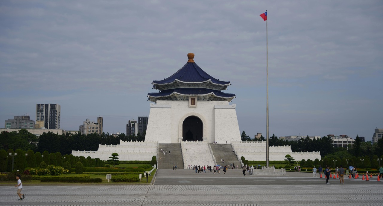 Chiang Kai-shek Memorial Hall in Taipei, Taiwan, with visitors walking up the steps and a tall flagpole displaying the Taiwanese flag.