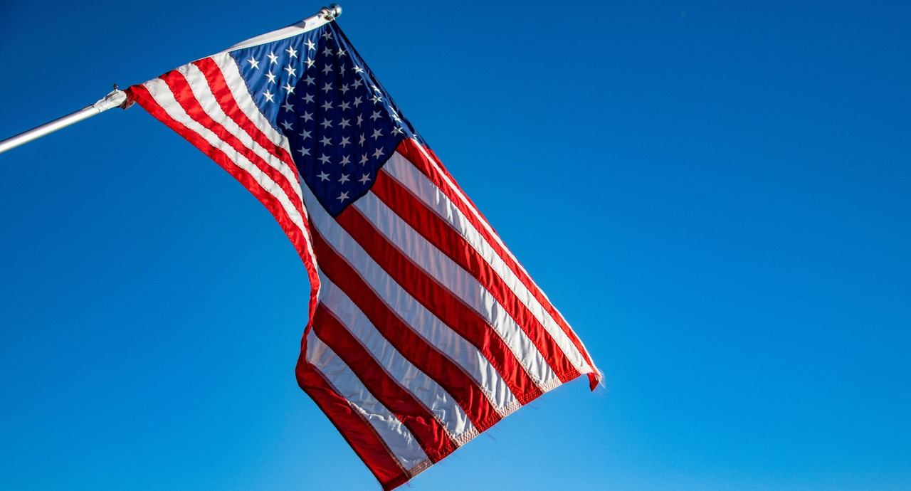 U.S. flag waving against a clear blue sky.