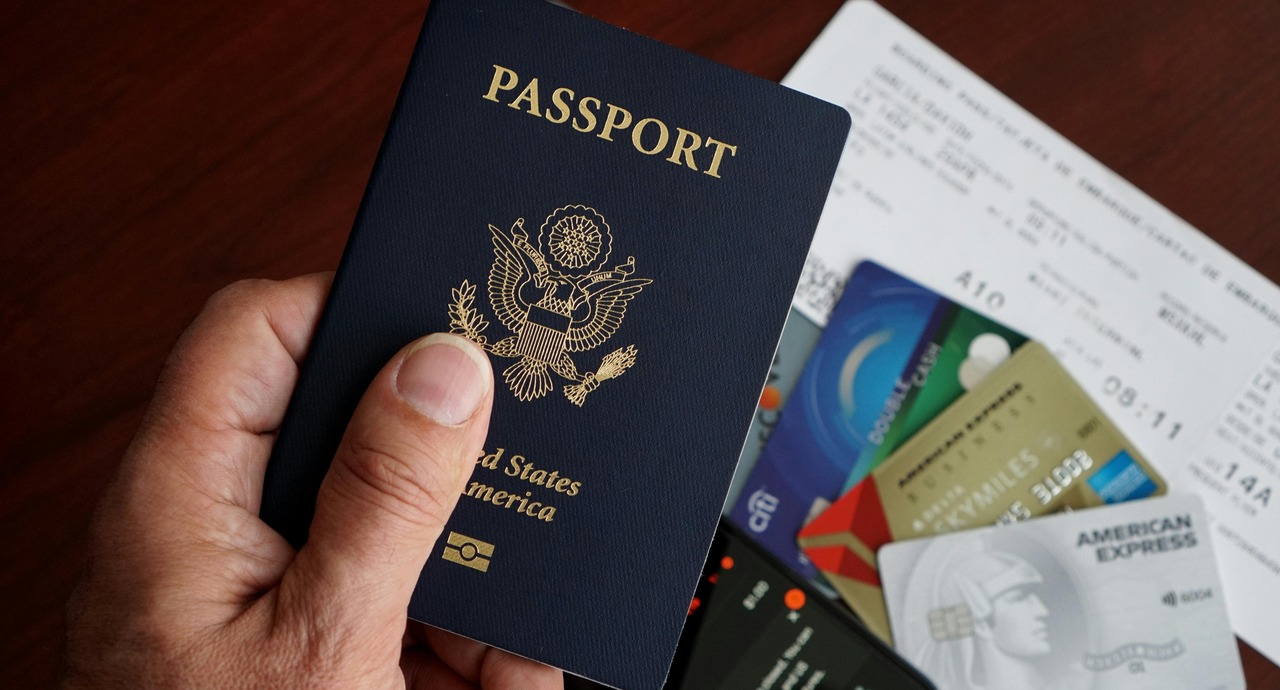 A person holding a U.S. passport with credit cards, a boarding pass, and other travel documents in the background.