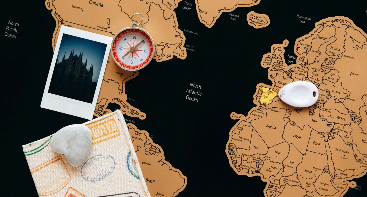 A close-up of a travel map with a compass, a photo, a white stone, and a map marker highlighting Spain. A close-up of a travel map with a compass, a photo, a white stone, and a map marker