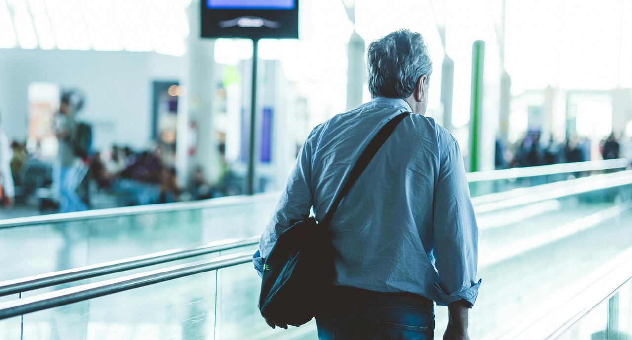 Man walking through an airport terminal with a shoulder bag.