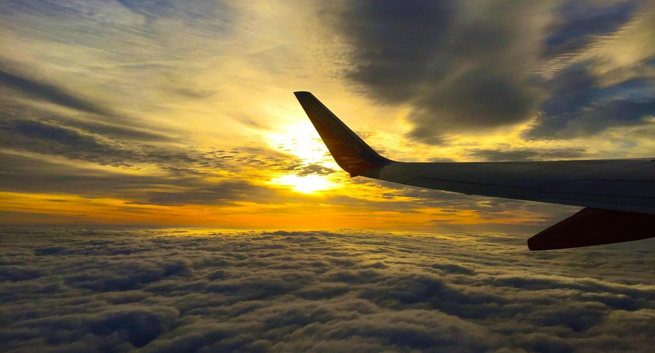 Airplane wing above a blanket of clouds during a vibrant golden sunset.