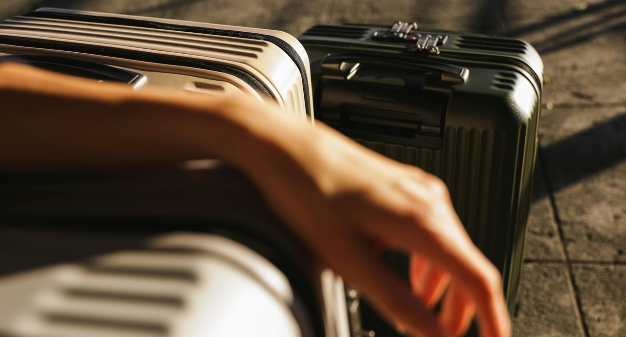 Close-up of a person’s arm resting on hard-shell suitcases in sunlight.