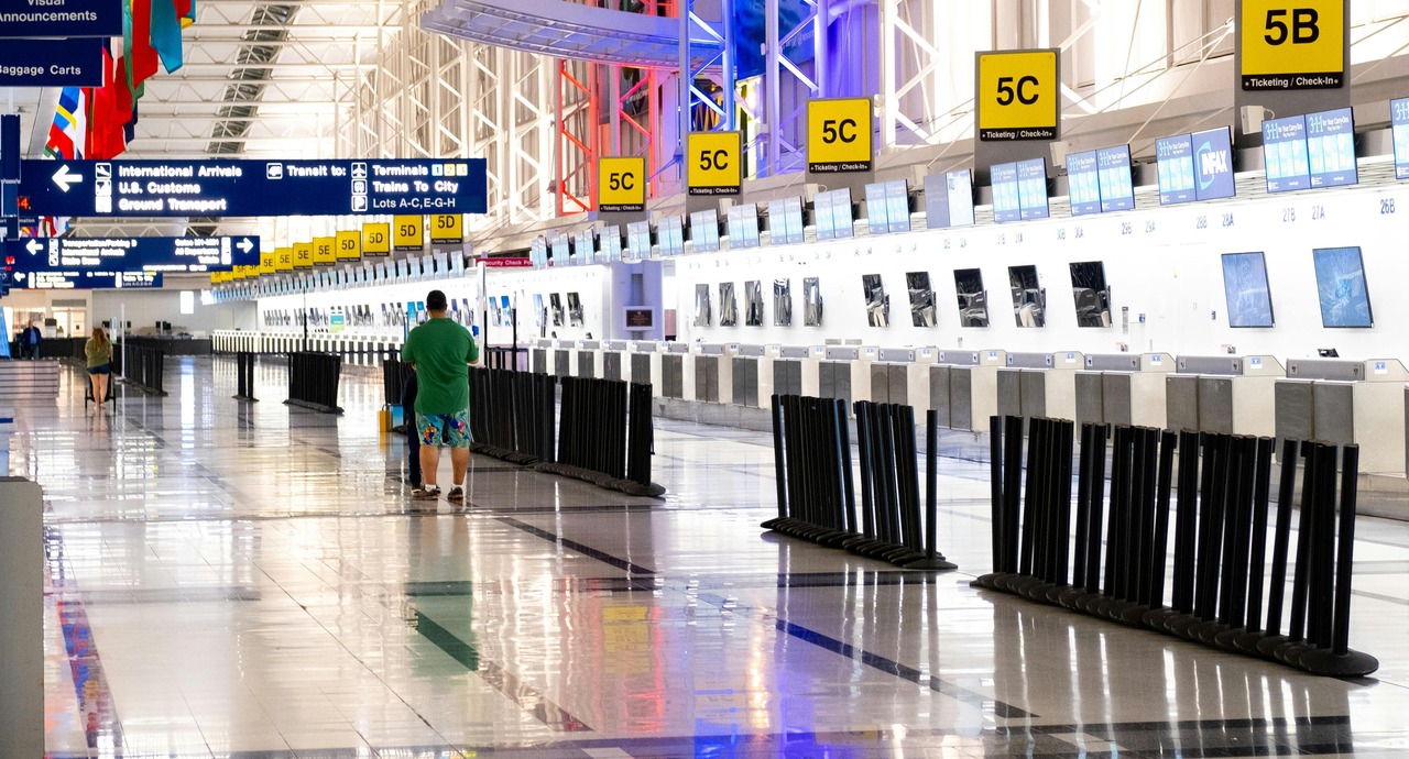 Nearly empty airport check-in area with two travelers walking toward ticket counters under yellow gate signs.