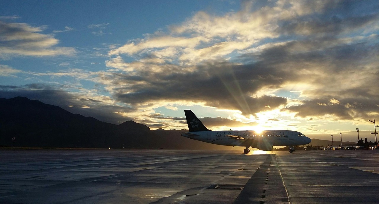 Airplane on a wet runway at sunset with mountains and dramatic clouds in the background.