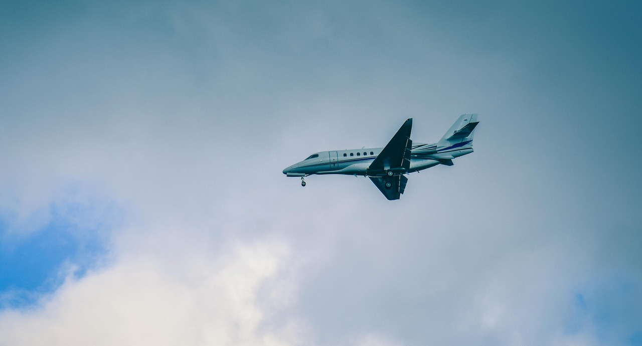 A small passenger jet flying through a cloudy sky with its landing gear extended.